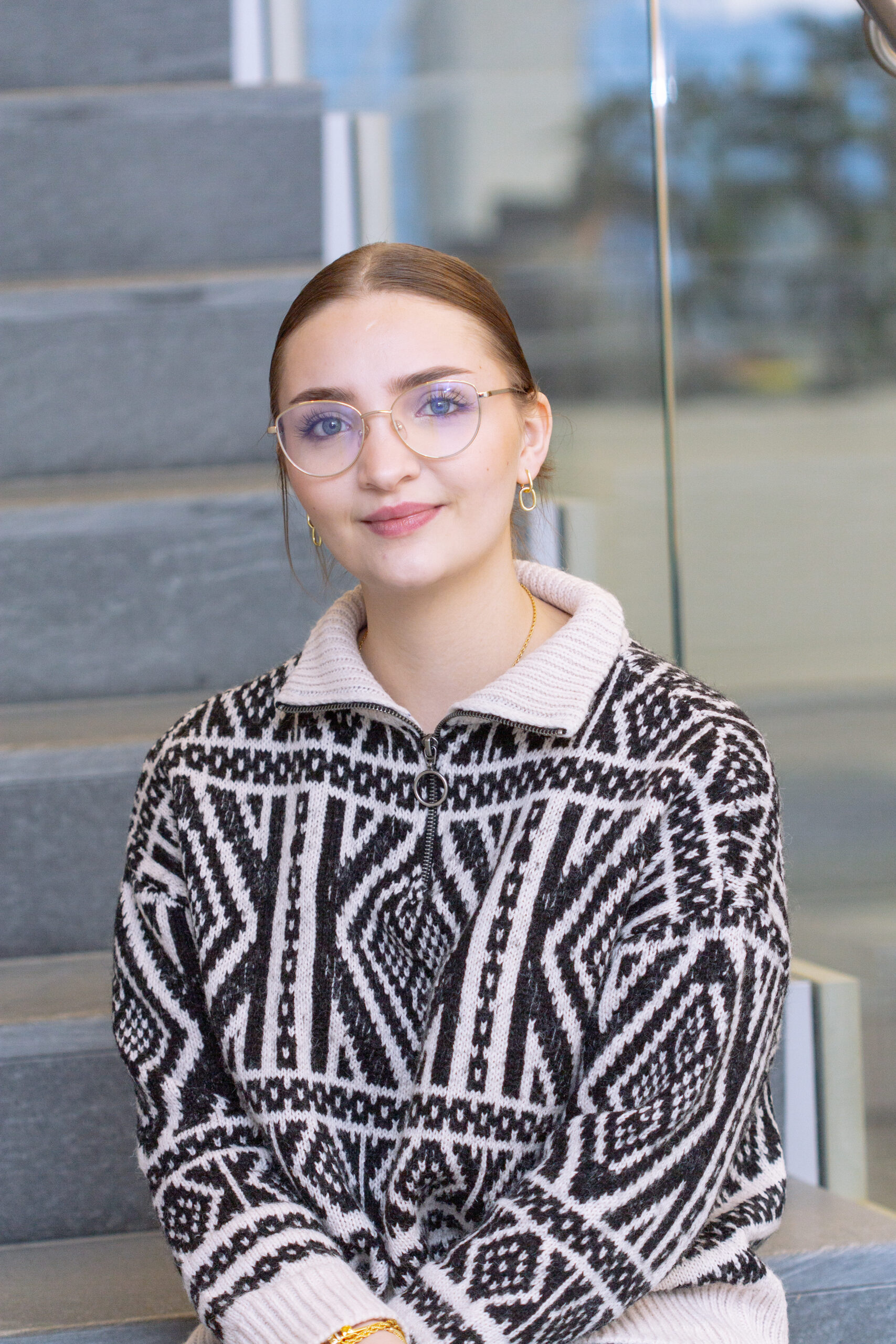 Die Redakteurin und Social Media Managerin Evelyn Halamov sitzt auf einer Treppenstufe, im Hintergrund ein helles Bürogebäude mit Glas und Grünpflanzen.